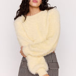 Woman wearing a light yellow fluffy sweater and striped skirt against a white background