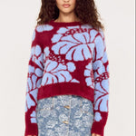 Woman wearing a red and blue floral-patterned sweater with a denim skirt on a white background