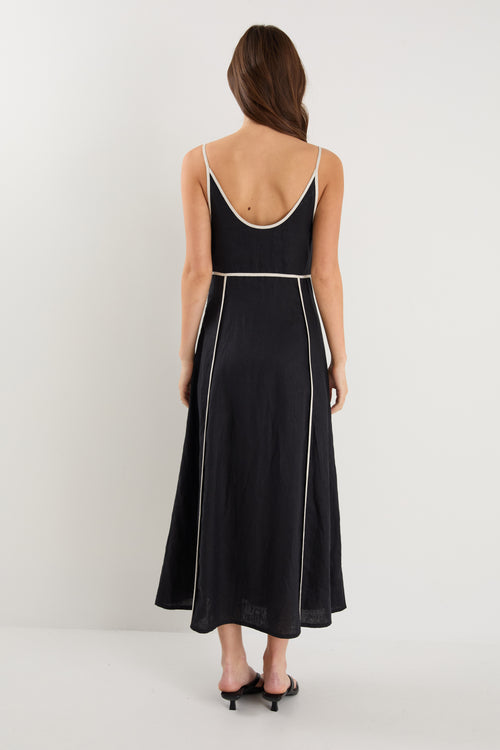 Woman wearing a black linen strappy dress with white contrast trim, fully lined, styled with black heeled sandals.