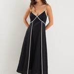 Woman wearing a black linen strappy dress with white contrast trim, fully lined, styled with black heeled sandals.