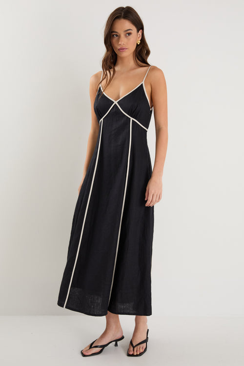 Woman wearing a black linen strappy dress with white contrast trim, fully lined, styled with black heeled sandals.