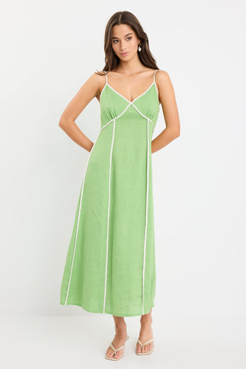 Woman wearing an apple green strappy linen maxi dress with cream contrast piping and flowy silhouette, styled with neutral sandals.