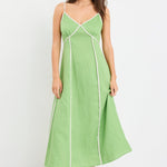 Woman wearing an apple green strappy linen maxi dress with cream contrast piping and flowy silhouette, styled with neutral sandals.