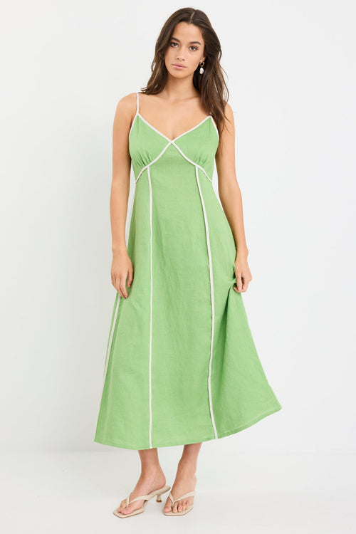 Woman wearing an apple green strappy linen maxi dress with cream contrast piping and flowy silhouette, styled with neutral sandals.