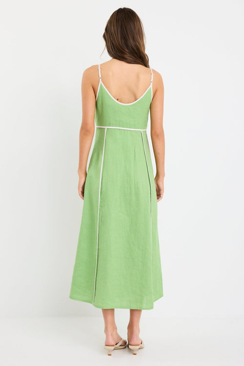 Woman wearing an apple green strappy linen maxi dress with cream contrast piping and flowy silhouette, styled with neutral sandals.