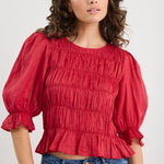 Woman wearing a red blouse with puffed sleeves and blue jeans on a white background