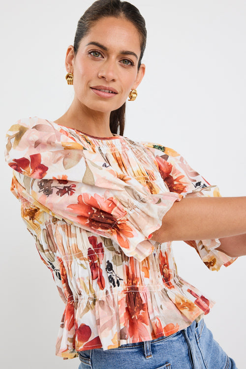 woman wearing a floral shirred short sleeve top with frill sleeves, styled with denim jeans and gold earrings.