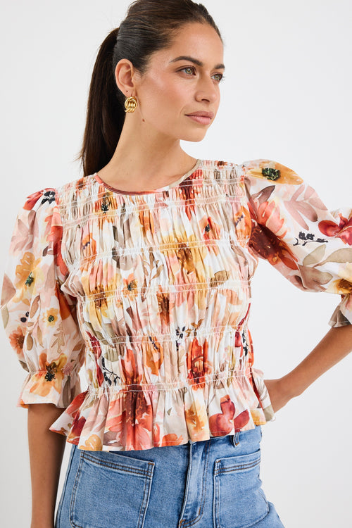 woman wearing a floral shirred short sleeve top with frill sleeves, styled with denim jeans and gold earrings.