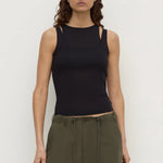 A woman modeling a black sleeveless knit top with cutout details at the shoulders and sides, paired with olive green pants, against a plain light gray studio background.