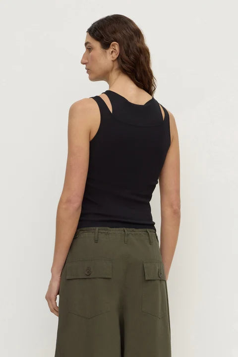 A woman shown from the back wearing a black sleeveless racerback tank top and olive green cargo pants against a plain light gray studio background.