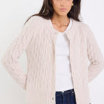 Woman wearing a beige cable knit cardigan over a white shirt with blue jeans on a white background