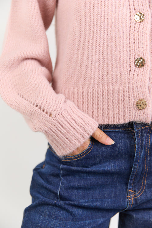 Pink knitted cardigan with gold buttons worn by a person, with a focus on the sleeve and hand.