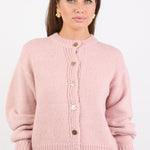 Woman wearing a pink cardigan with button details on a white background