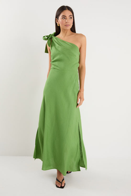 Model wears a one shoulder green midi dress with white heels