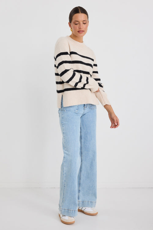 Woman wearing a cream and black striped funnel neck knit jumper, paired with light-wash wide-leg jeans and gold earrings.