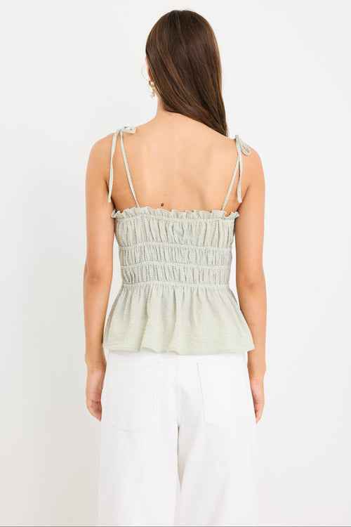 Woman wearing a sage green gingham strappy cami top with tie straps and an elasticated waist, styled with ecru jeans.