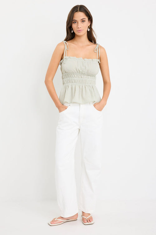Woman wearing a sage green gingham strappy cami top with tie straps and an elasticated waist, styled with ecru jeans.