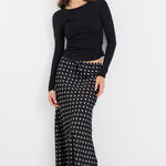 Woman wearing a black long-sleeve top and a black and white patterned skirt on a white background