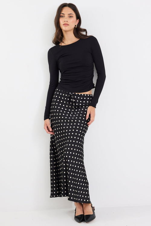 Woman wearing a black long-sleeve top and a black and white patterned skirt on a white background