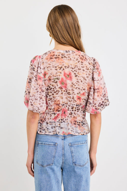 Woman wearing a short sleeve bubble blouse with a mix of floral and animal prints, button front, and elastic waist, styled with light blue jeans.