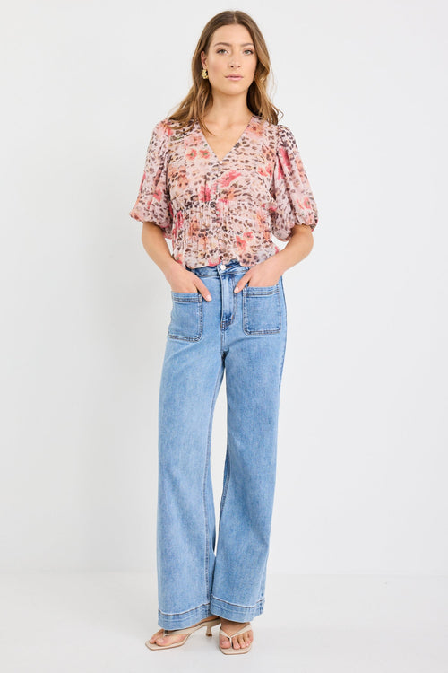 Woman wearing a short sleeve bubble blouse with a mix of floral and animal prints, button front, and elastic waist, styled with light blue jeans.