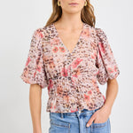 Woman wearing a short sleeve bubble blouse with a mix of floral and animal prints, button front, and elastic waist, styled with light blue jeans.