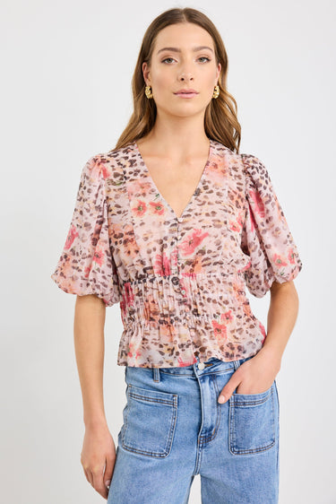 Woman wearing a short sleeve bubble blouse with a mix of floral and animal prints, button front, and elastic waist, styled with light blue jeans.