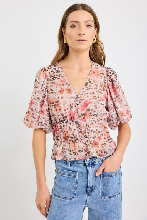 Woman wearing a short sleeve bubble blouse with a mix of floral and animal prints, button front, and elastic waist, styled with light blue jeans.