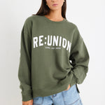 Woman wearing a khaki green oversized sweatshirt with "RE:UNION" printed across the chest, styled with light blue denim shorts.