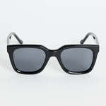 Glossy black rounded-square sunglasses with dark tinted lenses and RE:UNION label branding on the arm, photographed on a white background