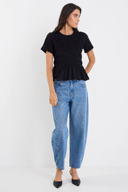 Woman wearing a black peplum top and blue jeans on a white background