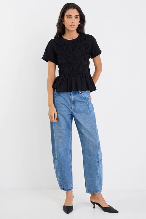 Woman wearing a black peplum top and blue jeans on a white background