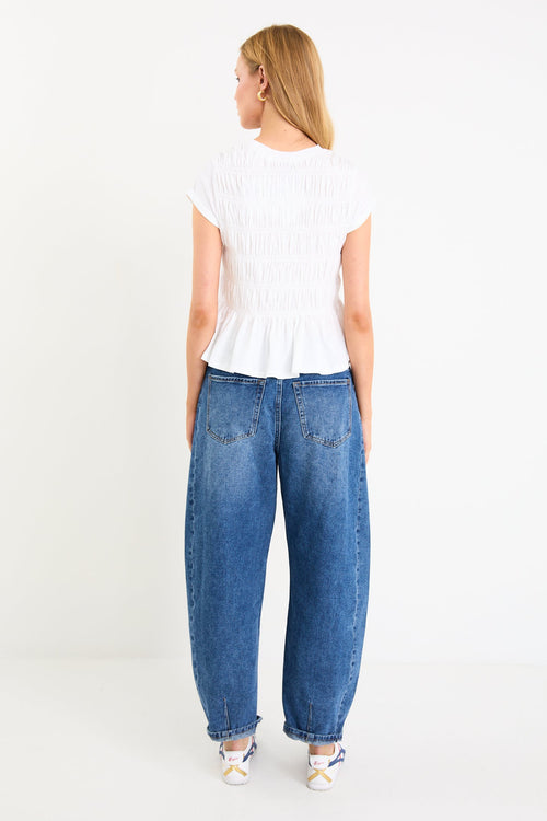 Model wearing a white short sleeve shirred cotton top with a peplum hem and crew neckline