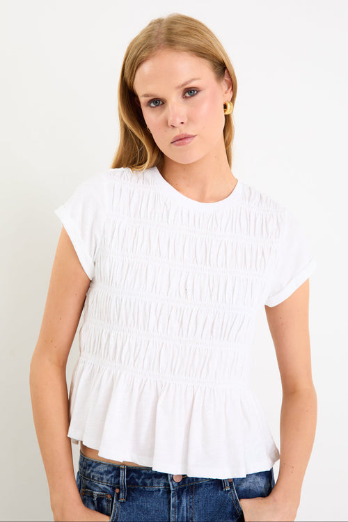 Model wearing a white short sleeve shirred cotton top with a peplum hem and crew neckline