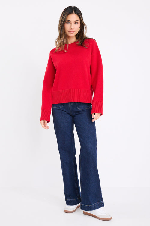 model wears a red knit jumper with dark blue jeans