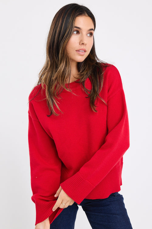 model wears a red knit jumper with dark blue jeans