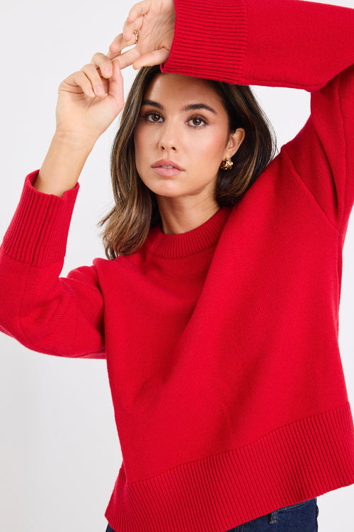 model wears a red knit jumper with dark blue jeans
