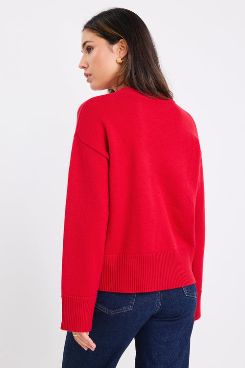 model wears a red knit jumper with dark blue jeans