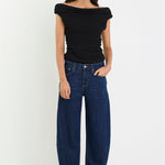 Woman wearing a black off-shoulder top and blue jeans on a white background