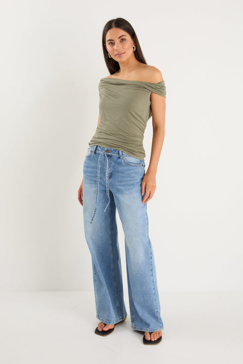Woman wearing an off-shoulder green top and light blue jeans on a white background