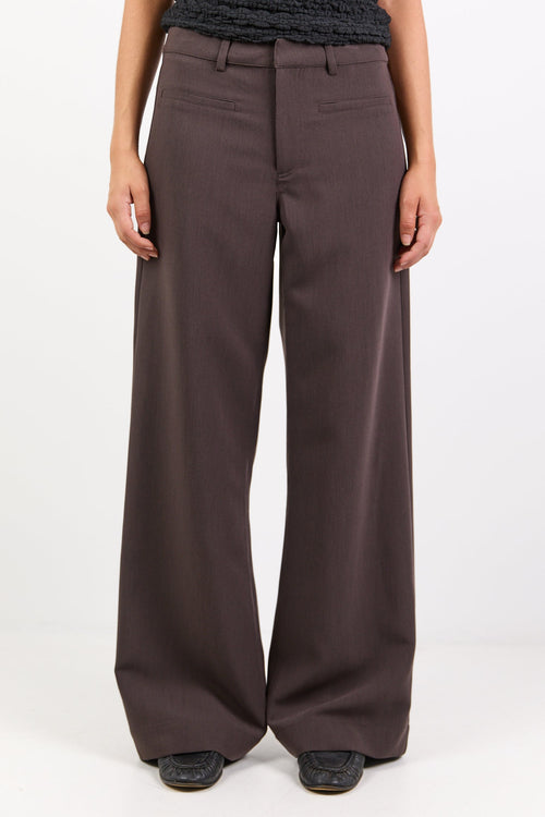Person wearing a black textured top and brown wide-leg pants on a white background