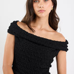 Woman wearing a black off-shoulder top against a white background