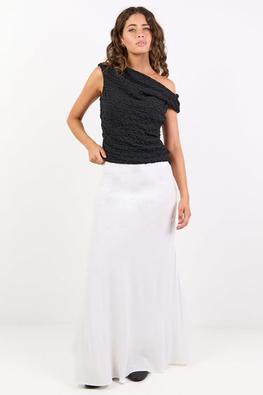 Woman wearing a black one-shoulder top and white pants on a white background