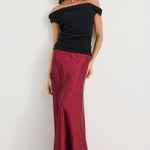 Woman wearing a black off-shoulder top and burgundy pants on a white background