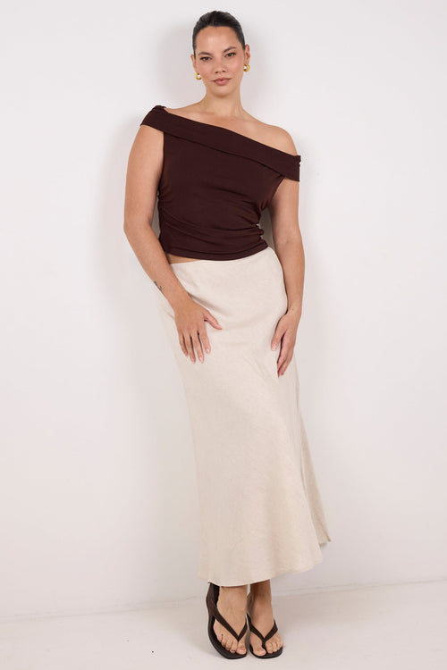 A woman modeling a dark brown off-the-shoulder top and a cream-colored midi skirt, paired with black strappy heels, against a plain white studio background.
