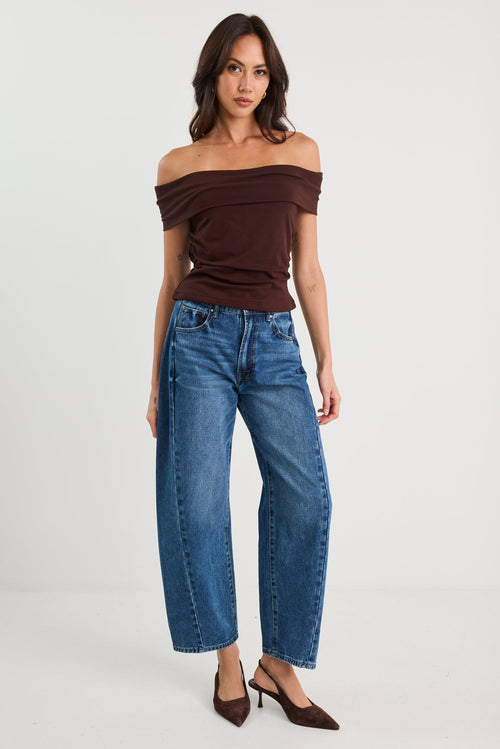 Woman wearing a brown off-shoulder top and blue jeans on a white background
