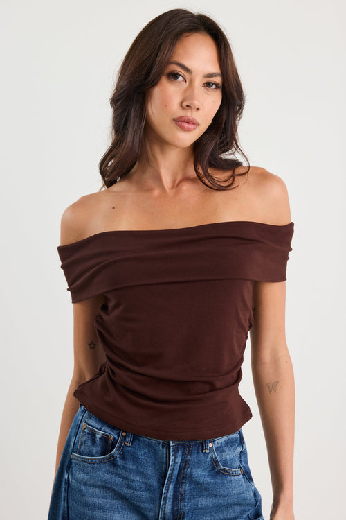 Woman wearing a brown off-shoulder top and blue jeans on a white background