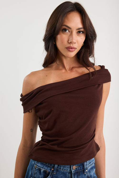 Woman wearing a brown off-shoulder top and blue jeans against a white background