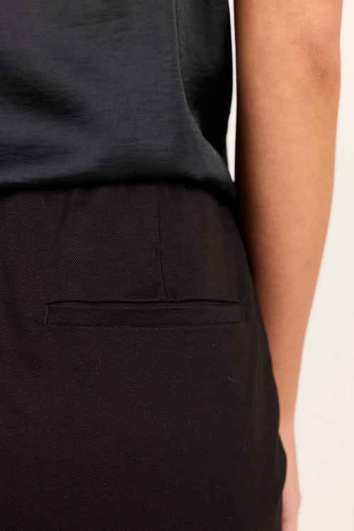 Close-up of a person wearing black trousers with a side pocket and a dark top, against a plain light background.