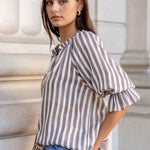 Woman in a striped shirt and jeans standing against classical architecture.